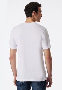 Hvid bomulds t-shirt med korte ærmer, klassisk rund halsudskæring og en afslappet pasform. Båret med blå jeans, set fra ryggen.