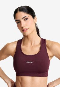 Burgundy sport-bh i slätt tyg, med scoop-halsringning, breda axelband och en vit logotyp på framsidan. Designen är figurnära och minimalistisk.
