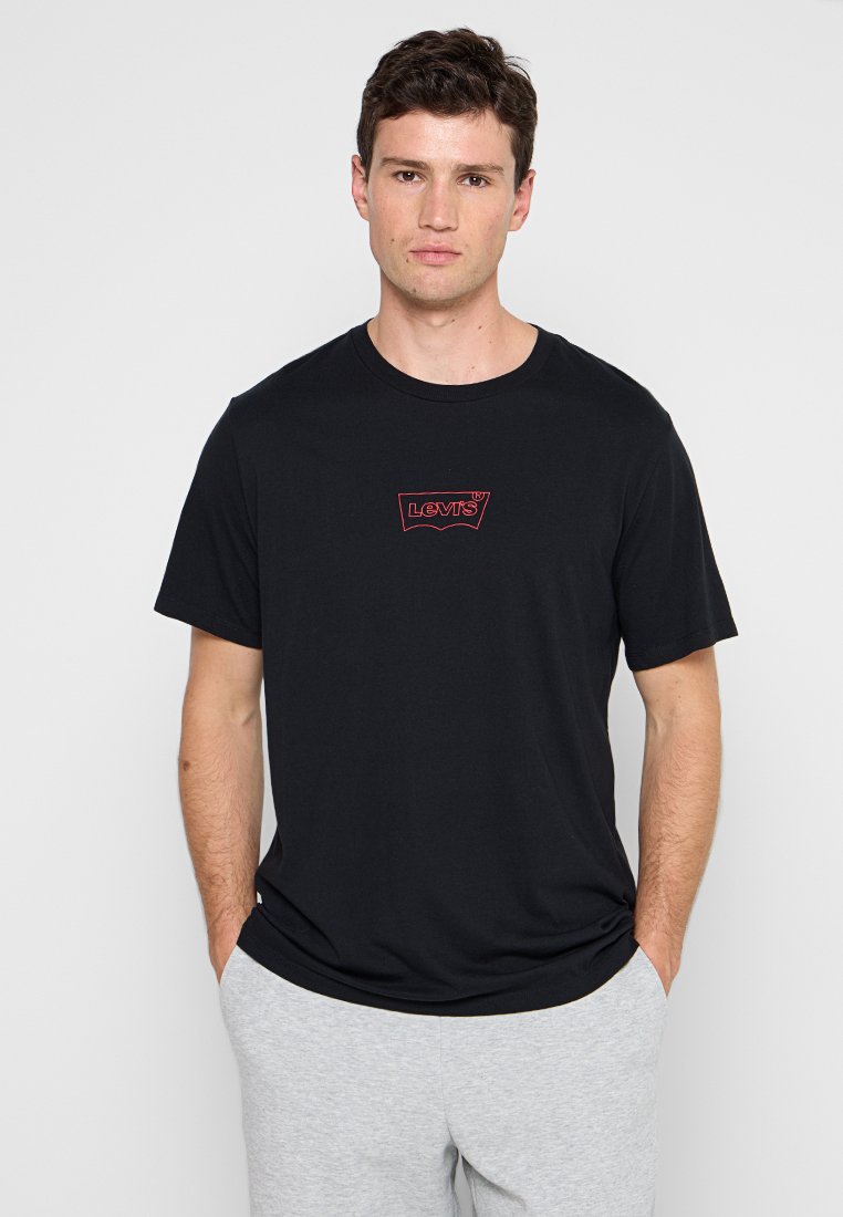 Schwarzes Baumwoll-T-Shirt mit Rundhalsausschnitt, mit einem kleinen roten Levi's-Logo auf der Brust. Das Modell trägt graue Jogginghosen.