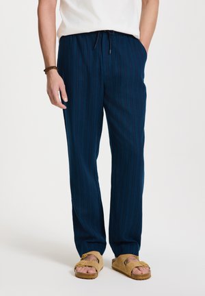 Navyblauwe gestreepte loungebroeken met een ontspannen pasvorm, een trekkoord in de taille en een zachte textuur, gecombineerd met lichtbruine sandalen.
