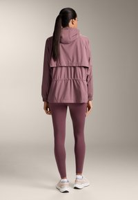Lichtpaarse windjack met capuchon, gelaagd ontwerp aan de achterkant, elastische manchetten; gecombineerd met bijpassende strakke leggings en lichte sneakers.