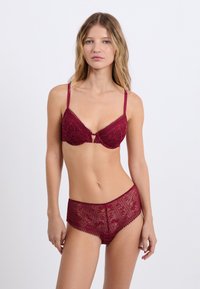 Mauve Spitzen-BH mit einem Schlüsselloch-Detail, verstellbaren Trägern und passenden hochsitztenden Spitzen-Höschen mit Blumenmustern und gewellten Kanten.