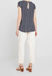 Top a righe blu navy e panna a maniche corte con schiena a chiave, abbinato a pantaloni tapered di colore chiaro e sandali con tacco a blocco marroni.