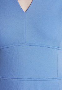 Jasnoniebieska sukienka z dekoltem w kształcie litery V, z teksturowanej tkaniny i widocznymi detalami szycia, w dopasowanym kroju.