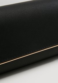 Gros plan d'un portefeuille en cuir noir avec une texture fine, des coutures visibles et une fine bordure métallique dorée le long du bord.
