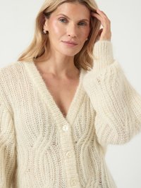 Jasnobeżowy sweter z dzianiny z dekoltem w serek, wyraźnym wzorem teksturowym, pięcioma guzikami i obszerne rękawy w miękkim, puszystym materiale.