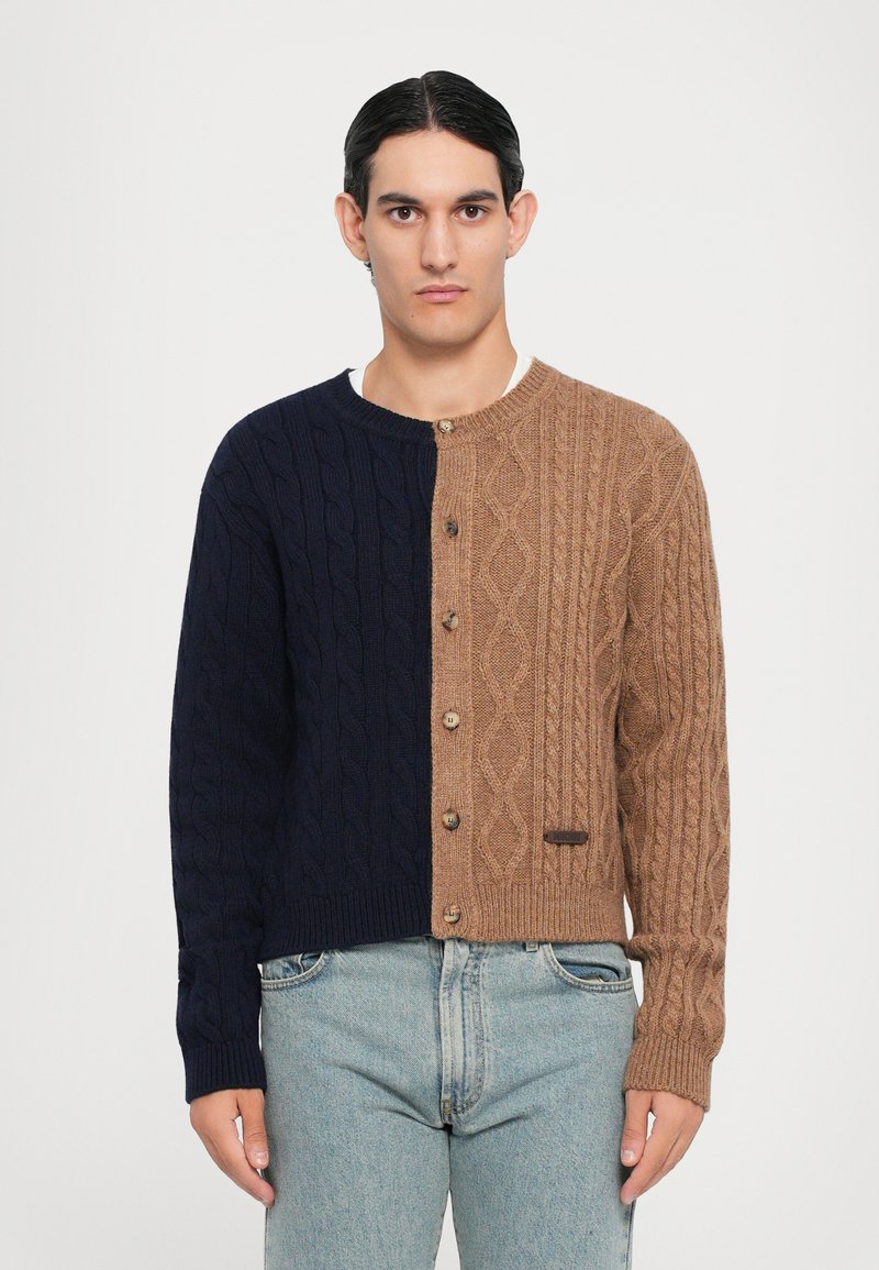 Färgblockerad cardigan med marinblått på vänster sida och ljusbrunt på höger. Kabelstickad textur med träknappar och en liten etikett.