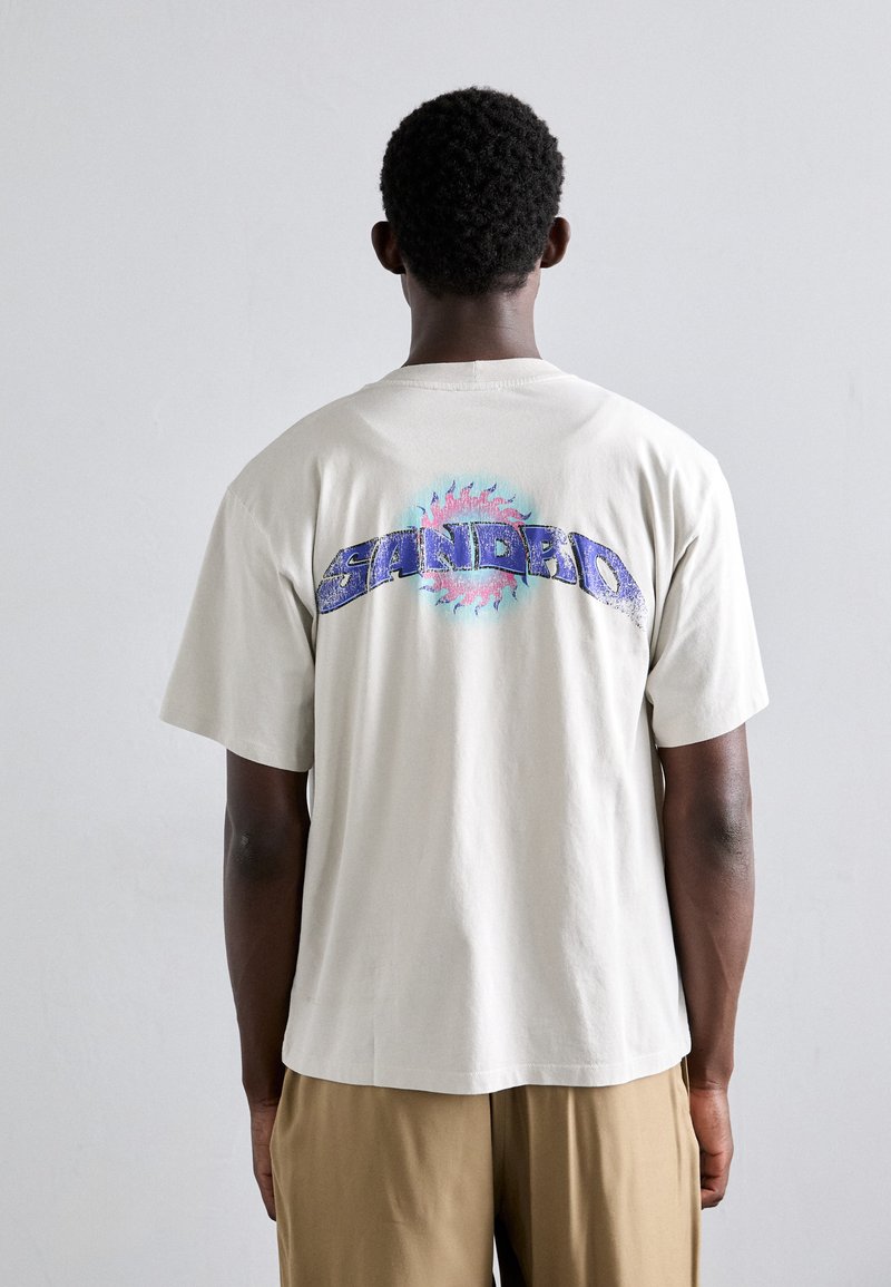 Short-sleeve cream t-shirt with a colorful printed design on the back, featuring the word "SANDRO" and a sun motif in blue and pink tones.