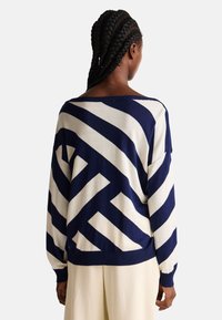 Oversized svetr v námořnické modři a smetanové barvě s diagonálními pruhy. Disponuje širokým výstřihem a žebrovanými manžetami. Měkká pletená textura.