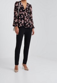 Blusa negra con flores rosas, escote en V y detalle de lazo, combinada con pantalones negros ajustados y zapatos de tacón nude. Incluye un bolso sencillo.