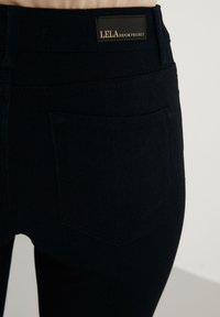 Jeans de mezclilla oscura con una textura suave, que cuentan con un bolsillo trasero y una etiqueta de cuero de marca que dice "LELA DENIM PROJECT."