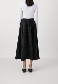 Falda larga negra de tejido con ojales y patrones troquelados, cintura elástica y diseño fluido, combinada con zuecos negros.