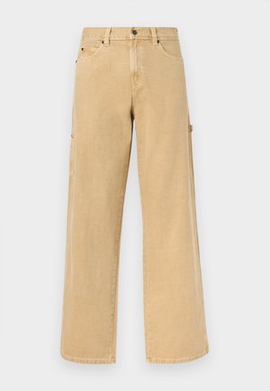 Taisnas bēša darba bikses ar jostas cilpām, priekšējām un sānu kabatām, kā arī āmura cilpu uz vienkārša fona.