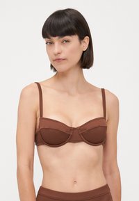 Brun ribbet bikinitopp med en strukturert, underbøyd design. Har tynne justerbare stropper og en horisontal søm over koppene.