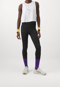 Valkoinen lyhythihainen toppi, jossa on printtisuunnittelu, mustat leggingsit, joissa on pyörrekuvio, violetit nilkkasukat ja valkoiset urheilukengät.