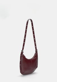 Borsa hobo in pelle di un profondo bordeaux, con forma arrotondata, chiusura con zip e tracolla chiodata. Presenta una texture liscia e accenti metallici.