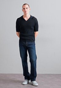 Black short-sleeve knit sweater with a V-neck, paired with dark blue jeans and white sneakers. Simple design with a textured finish.