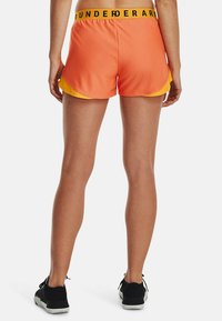 Orangea och gula sportshorts med svart logoband i midjan. Designen har en lager-på-lager-effekt och en rundad fåll för rörelsefrihet.