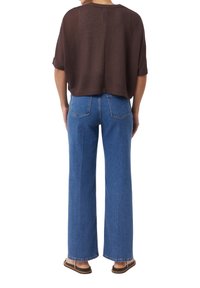 Bruine korteknuffel trui met korte mouwen, gecombineerd met blauwe wijde spijkerjeans. De top heeft een losse pasvorm, en de jeans hebben achterzakken en een hoge taille.