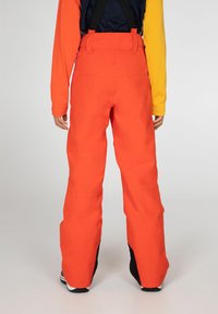 Oranje sneeuwbroeken met verstelbare zwarte banden, brede pijpen en zwarte accenten aan de randen. Gladde textuur en duurzaam materiaal.