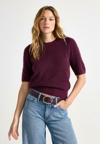 Kortærmet, burgundy striktrøje med et struktureret mønster, parret med højtaljede lysblå jeans og et mørkt bælte med en guldbuckle.