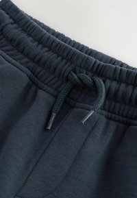 Pantalons de survêtement bleu marine avec une taille élastique côtelée et un cordon de serrage tressé. Caractéristiques d'un tissu lisse et de poches latérales.