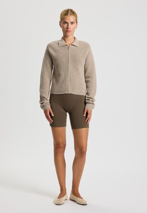 Beige pruhovaný pletený svetr na zip s límečkem, zkombinovaný s hnědými šortkami a tkanými slip-on botami, s hladkou texturou.