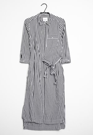 Black and white vertical striped long-sleeve shirt dress with collar, chest pocket, waist tie, and buttons, hanging on black hanger.