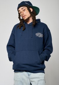 Sweatshirt à capuche bleu marine avec poche avant et cordons de serrage. Présente le logo "Kaporal" en blanc sur la poitrine. Tissu doux et coupe décontractée.