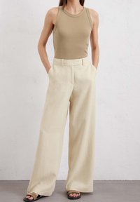 Top de tirantes ajustado de color beige, con pantalones de talle alto y anchos de color crema que tienen una textura suave y un corte relajado, combinados con sandalias negras.