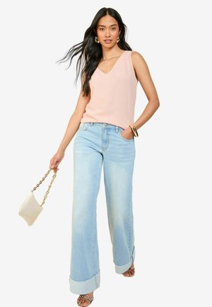 Haut sans manches rose clair avec un col en V, associé à un jean bleu clair à pattes d'éléphant. Les accessoires comprennent un sac à main crème avec une bandoulière en chaîne dorée.