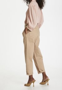 Beige Leinenhosen mit hochgerollten Säumen, kombiniert mit einer hellrosa strukturierten Bluse und nude-farbenen Sandalen mit offenen Zehen.
