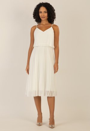 Weißes plissiertes Kleid mit V-Ausschnitt und dünnen Trägern, zeichnet sich durch eine fließende Silhouette aus, die bis zur Wade fällt. Silberne Akzente an den Trägern.