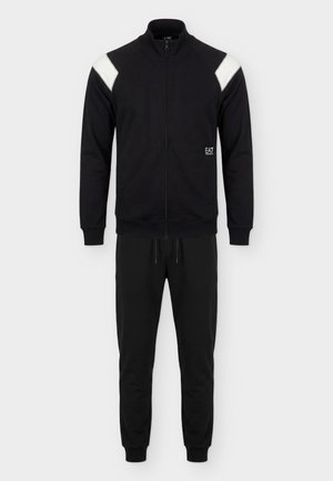 Schwarzer Trainingsanzug mit Reißverschluss, weißen Schulterpaneelen, gerippten Bündchen, Jogginghose mit Kordelzug und kleinem „EA7 Emporio Armani“ Logo auf der Jackenvorderseite.