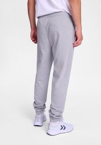 Graue Sweatpants aus strukturiertem Stoff, mit elastischem Bund und schmal zulaufenden Bündchen, kombiniert mit weißen Sportschuhen mit schwarzen Akzenten.