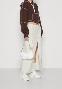 Brown cropped hoodie with contrasting stitching, beige cargo skirt with pockets and a slit, and a white handbag with a chain strap. White sneakers.