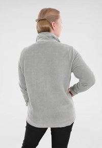 Lange mouwen, lichtgrijze corduroy top met een hoge kraag, ribbelstructuur en een rechte zoom. Draagt een zwarte broek, gezien van achteren.