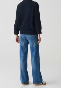 Pull texturé marine à manches trois-quarts associé à un jean bleu évasé avec poches arrière et décoloration subtile.