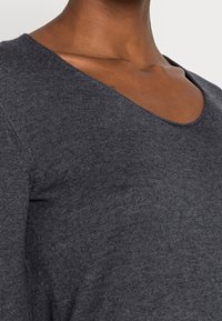 Pull en maille gris foncé avec un col en V, une texture fine et une silhouette ajustée, mettant en valeur le décolleté et la zone des épaules.