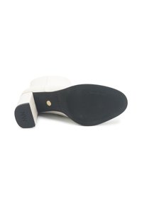 Botă albă cu toc înalt, cu vârful pătrat și o suprafață texturată. Are o talpă din cauciuc negru cu un branding subtil și un detaliu aurit.