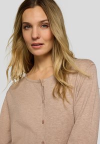 Hellbrauner Cardigan mit rundem Ausschnitt, langen Ärmeln und kleinen Knöpfen vorne. Hergestellt aus weichem, strukturiertem Stoff.