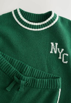 Groene trui en bijpassende broek, gemaakt van zacht materiaal. Voorzien van een witte gestreepte kraag en "NYC" borduursel aan de voorkant.