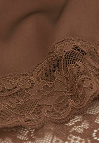 Brun tyg med en slät textur, prydt med intrikata spetsdetaljer längs kanten, som visar blommönster och en delikat nätdesign.