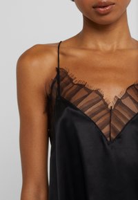 Camisón de satén negro con un escote de encaje a rayas transparente, delicados flecos y finas tirantes. Textura suave con un diseño en forma de V.