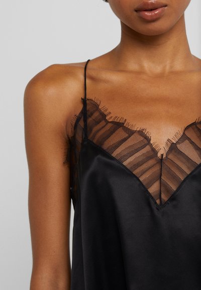 Black satin camisole featuring a sheer striped lace neckline, delicate fringing, and thin spaghetti straps. Smooth texture with a V-cut design.
