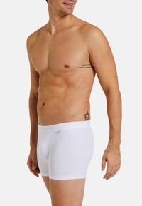 White cotton boxers with a soft waistband, featuring a snug fit and smooth texture, shown on a male model with no shirt.