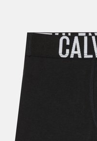Boxer shorts en coton noir avec une large ceinture élastique portant le texte "CALVIN KLEIN" en blanc. Texture lisse, design ajusté.