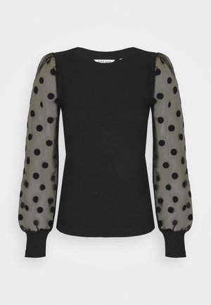Haut noir ajusté avec manches longues bouffantes en voile transparent à gros pois noirs et poignets côtelés.