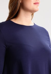 Granatowa, długosleeve'owa bluzka z gładkiego, lekkiego materiału, z okrągłym dekoltem i prostym wzornictwem. Brak widocznych wzorów lub akcentów.