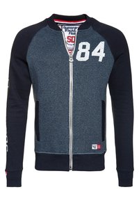 Marinblå zip-up sweatshirt med grå kropp, ribbade mudd och nederkant. Har nummer "84" på framsidan, sidofickor och en logotyp patch vid nederkant.